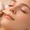 Esteticista aplicando cera depilatoria caliente en labio superior con espátula pequeña